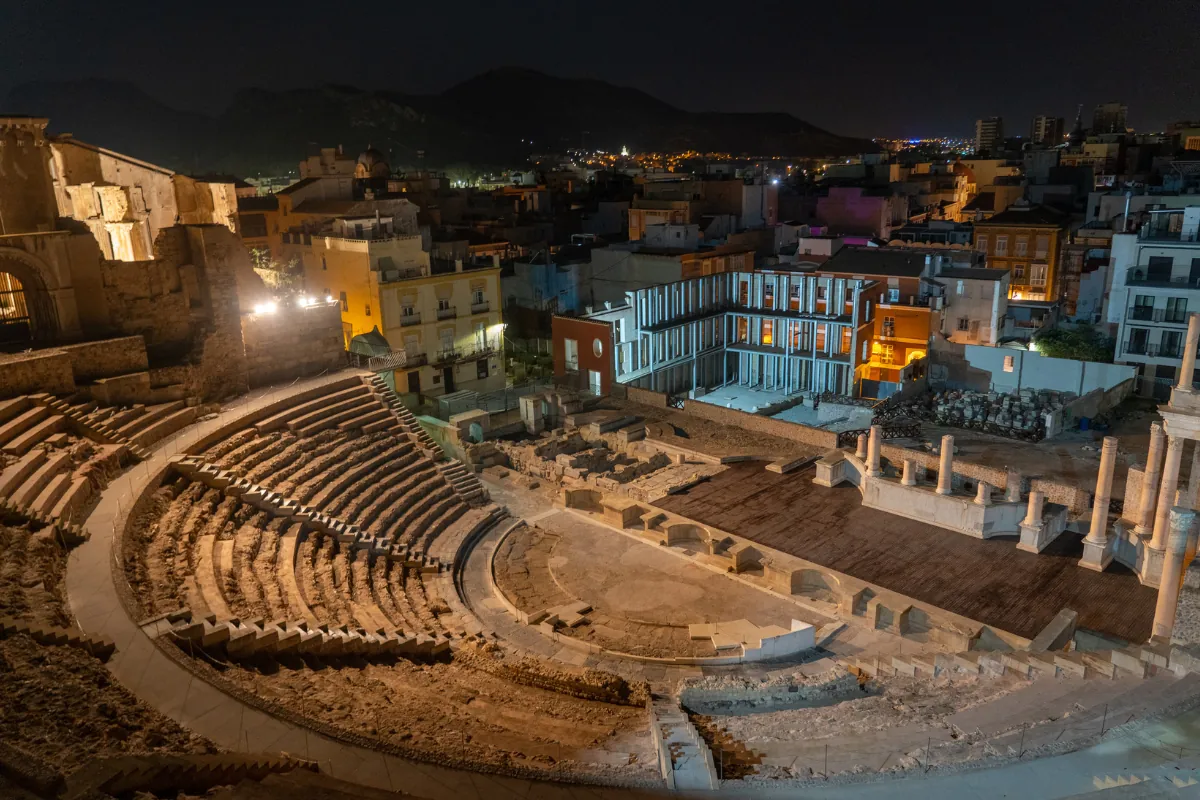El Teatro Romano de Cartagena iluminado de noche con la ciudad al fondo